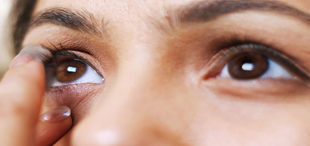 Imagine de aproape a ochiului unei tinere femei care își pune lentile de contact.
